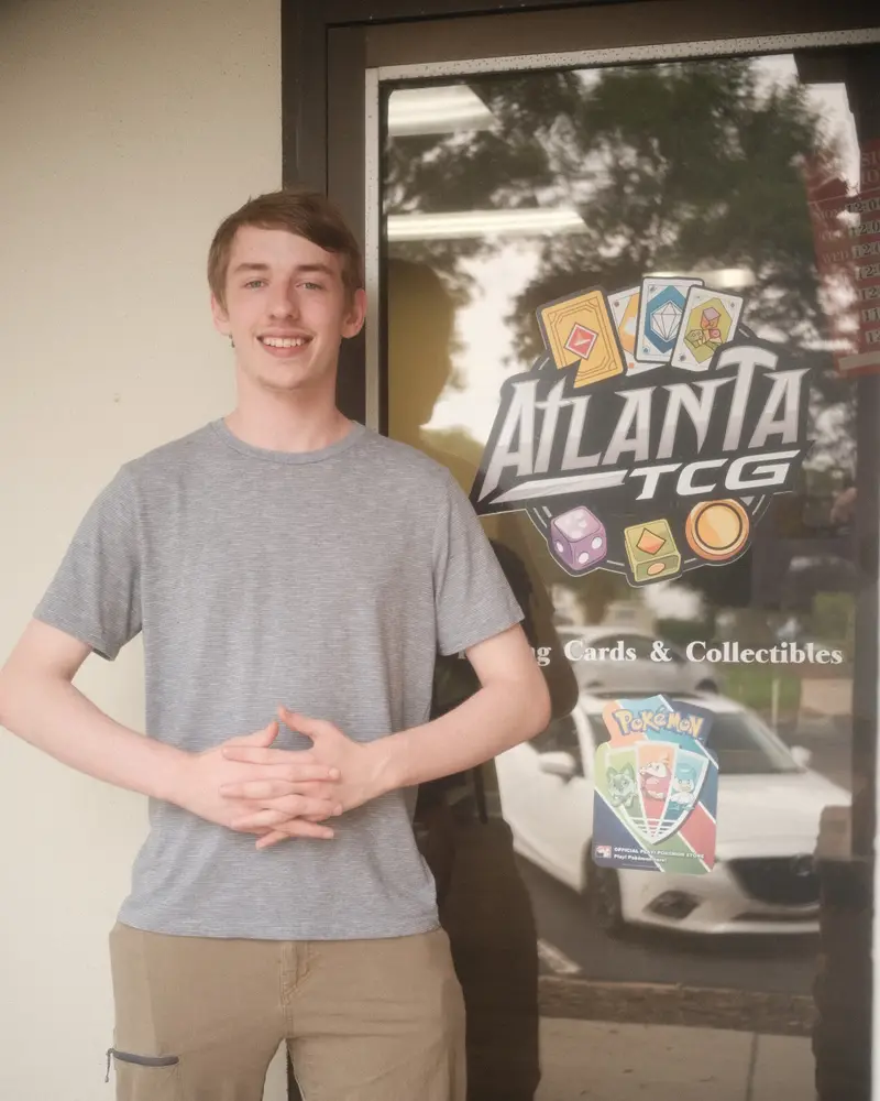 Logan at the front door of AtlantaTCG, under the shop logo